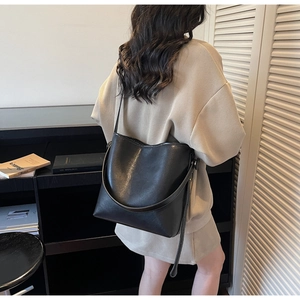 Detail of black leather bucket bag with white stitching and adjustable strap on a model
