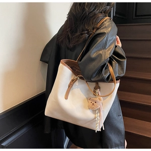 Detail of beige leather tote bag with brown straps and a cute plush teddy bear charm