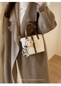 Detail of cream white tote bag with brown trim, leather handles and a cute bear charm