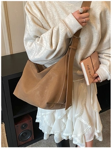 Brown faux suede tote bag with adjustable wide strap shown on model in cozy home setting
