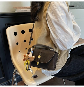 Brown matte leather crossbody bag with a gold clasp and a cute bear charm on a model