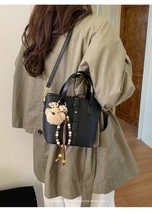 Detail of black lychee grain leather bucket bag with cute bear charm and bead accessory