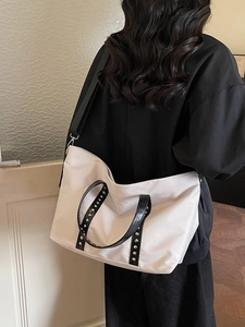 Grand sac cabas beige avec poignées à rivets noires et bandoulière porté par un modèle