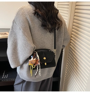 Rear view of model wearing black matte crossbody bag with cute bear charm and gold lock