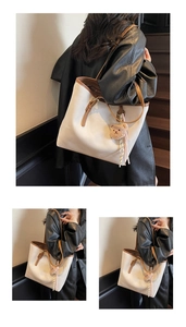 Detail of cream tote bag with brown trim, featuring a cute plush bear charm accessory