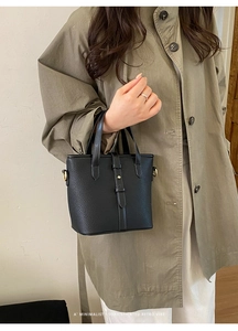 Detail of black lychee grain leather handbag with gold hardware and buckle strap
