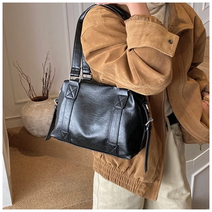 Detail of black faux leather tote bag with cross-stitch straps and metallic buckle