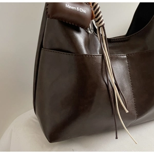 Détail du sac hobo en cuir marron foncé avec bandoulière tressée et logo de marque