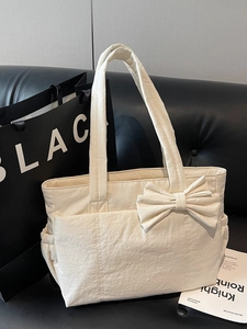 Grand sac fourre-tout beige avec nœud décoratif et plusieurs poches sur un canapé