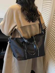 Sac fourre-tout noir à rivets avec bandoulière porté sur un trench-coat kaki