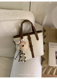Detail of cream-colored pebble leather bucket bag with brown handles and bear charm