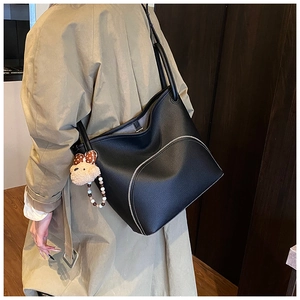 Close-up of black leather tote bag with unique curved zipper and plush bear charm