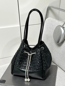 Chic black woven bucket bag with silver chain and pearl details on a desk