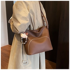 Detail view of coffee brown lychee leather tote bag with stylish bear charm and metal zipper