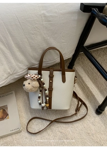 Litchi pattern bucket bag with bear pendant and adjustable strap on a cozy rug