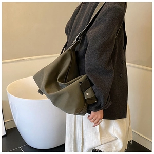 Detailed side view of an olive green oversized suede tote bag worn by a model