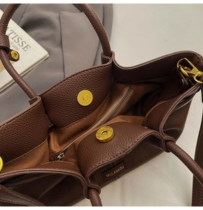Detail view of dark brown pebbled leather handbag with magnetic closure and gold hardware