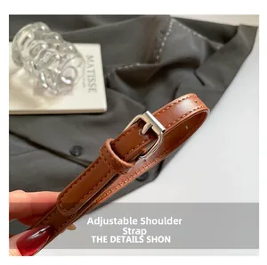 Detail of adjustable brown leather shoulder strap with silver metal buckle and stitching