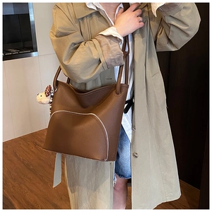 Detail view of brown pebbled leather bucket bag with semi-circular pocket and plush bear charm