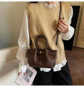 Detail of dark brown lychee leather handbag with golden twist-lock and soft drape