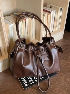 Deep brown bucket bag with drawstring closure and star charm next to books