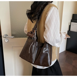 Détail d'un sac cabas en cuir souple marron foncé avec un pendentif décoratif de marque