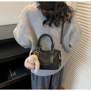 Detail of black woven crossbody bag with leather strap and cute rabbit plush charm