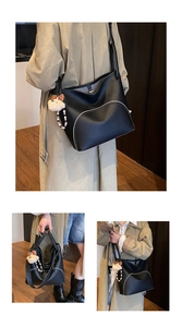 Detail of black lychee grain leather tote with curved zipper and plush bear charm