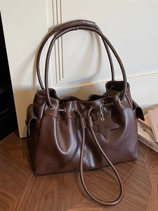 Vintage dark brown drawstring bucket bag with star charm on a rustic wooden background
