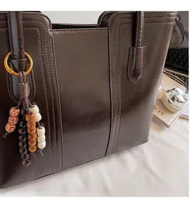 Detailed macro view of dark coffee glossy leather tote bag with wooden bead tassel charm
