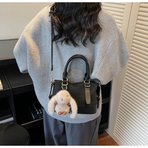 Detail of black woven texture shoulder bag with beige plush bunny charm on model
