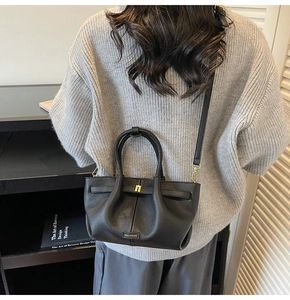 Detail of black pebbled leather bucket bag with top handle and gold metal brand hardware