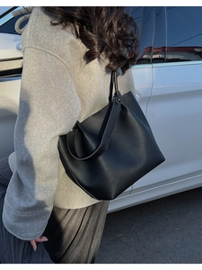Close-up of black lychee grain leather bucket bag with wide shoulder strap on model