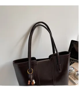 Detail of dark brown tote bag with fringe charm on a desk with office accessories