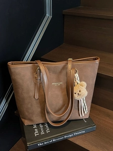 Vintage brown matte tote bag with shoulder straps and plush bear charm on wooden stairs