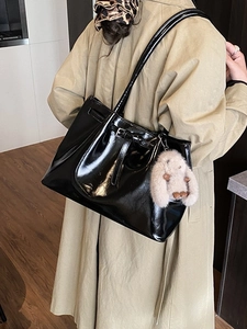 Grand sac cabas noir brillant avec porte-clé lapin porté par un mannequin en trench