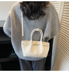 Close-up of white lychee grain tote bag with gold hardware and logo on model shoulder