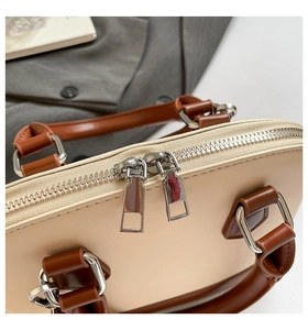 Detailed close-up of the silver double zipper and D-ring on the cream shell bag