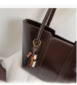 Detail of dark brown tote bag with glossy leather finish and colorful wooden beads charm