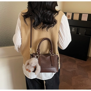Detail of dark brown woven pillow bag with golden hardware and plush rabbit charm