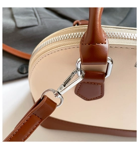 Close-up of silver metal hooks and stitching on a beige and brown leather handbag