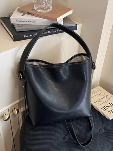 Chic black bucket bag with contrast stitching and wide strap on minimalist background