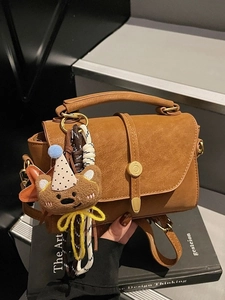 Brown matte leather tote bag with gold buckle and bear charm on vintage books