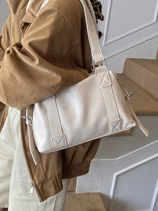 Chic cream tote bag with wide decorative straps shown on model in a modern interior
