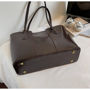 Close-up of deep brown glossy leather tote bag with protective gold metal feet on base