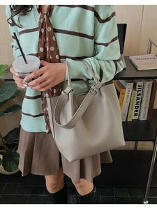 Detail of grey pebble leather tote bag shown with casual attire in minimalist setting