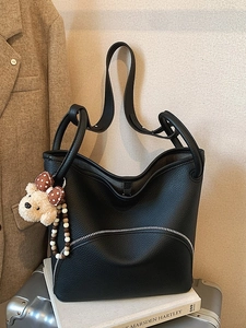 Black pebbled leather tote bag with silver zipper and brown teddy bear charm on luggage