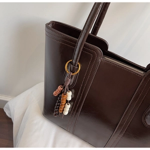 Detailed macro view of dark brown faux leather tote bag with stylish beaded tassel charm