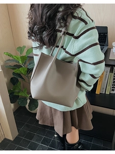 Lifestyle shot of grey pebbled leather bucket bag worn by model in cozy home setting