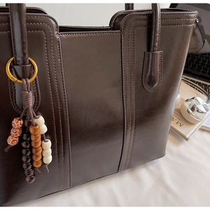 Detail of dark brown tote bag with smooth finish and beaded charm in a desk setting